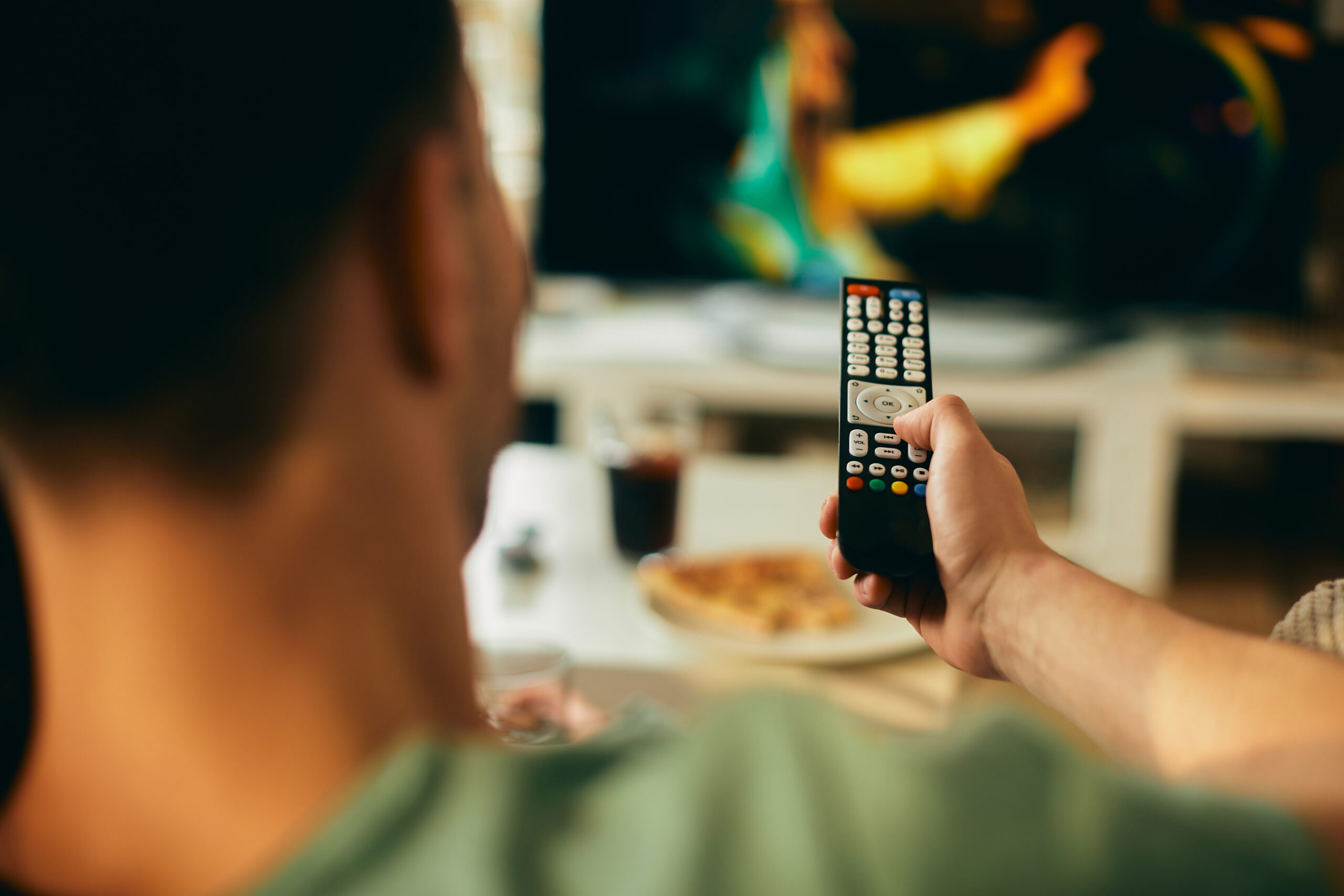 Photo of a young man watching television at home with the remote control in his hand