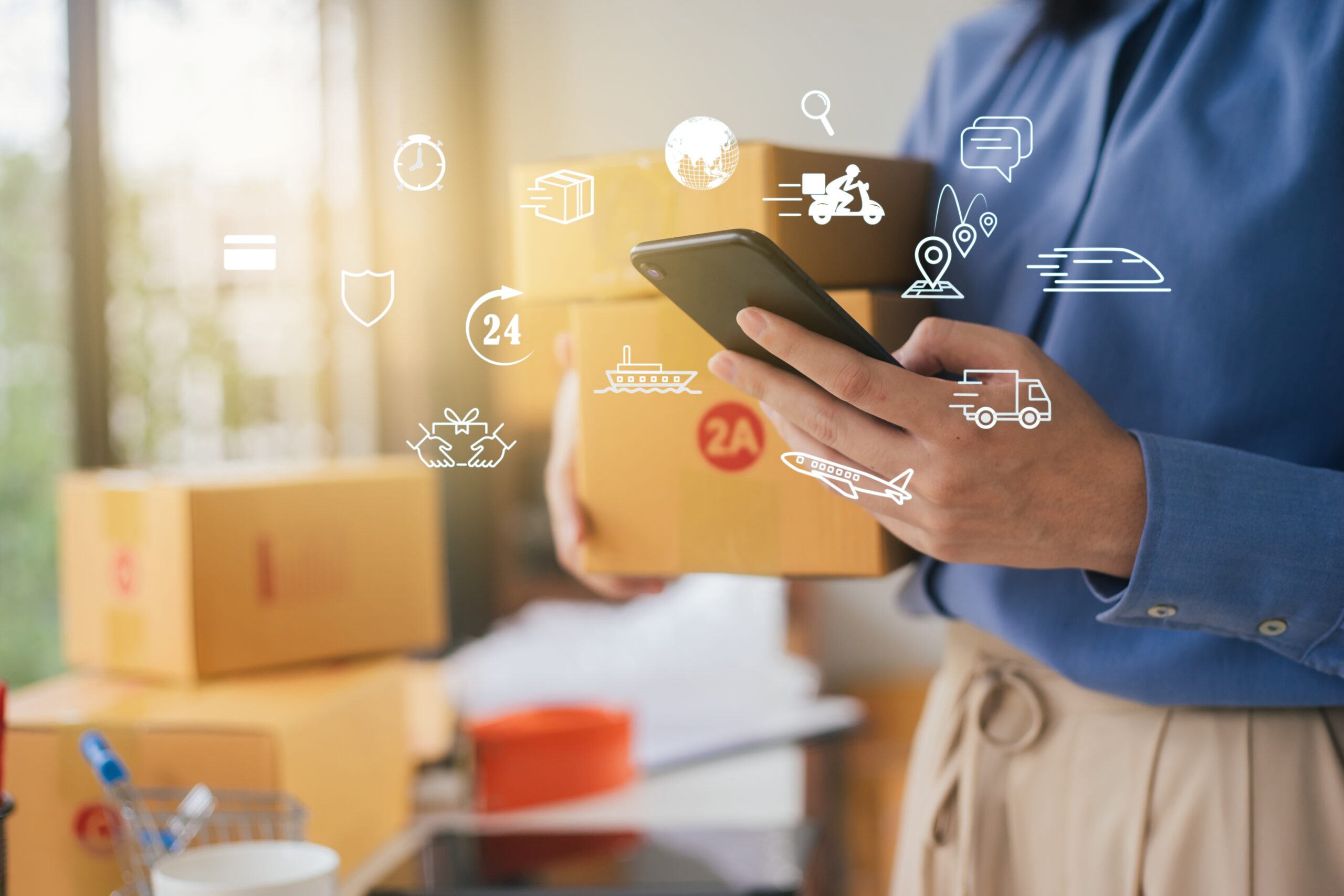 Illustrative photo of a person standing next to several parcels, holding a smartphone to manage shipments or the receipt of parcels