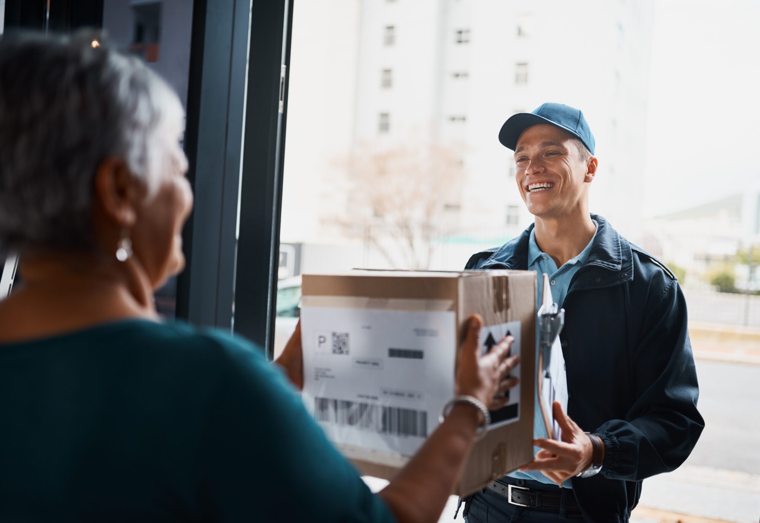 Photo of a delivery driver handing a parcel to an elderly lady at the entrance to her house 