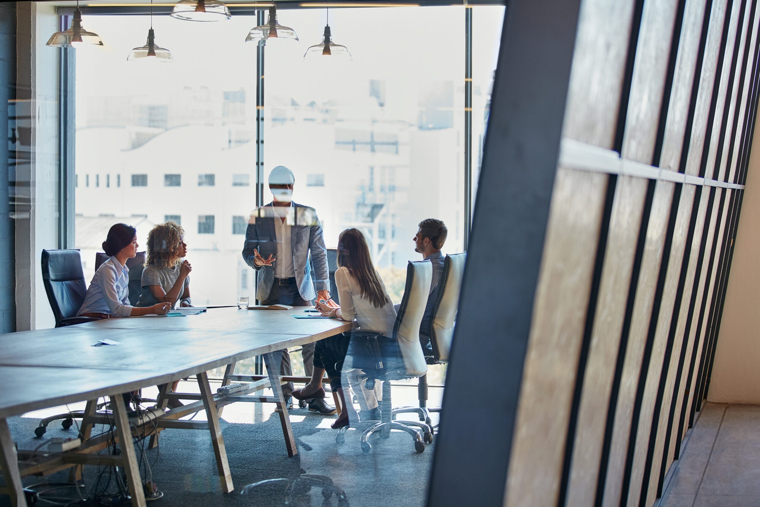 Illustrative photo of a meeting in a large meeting room with five people around the table 