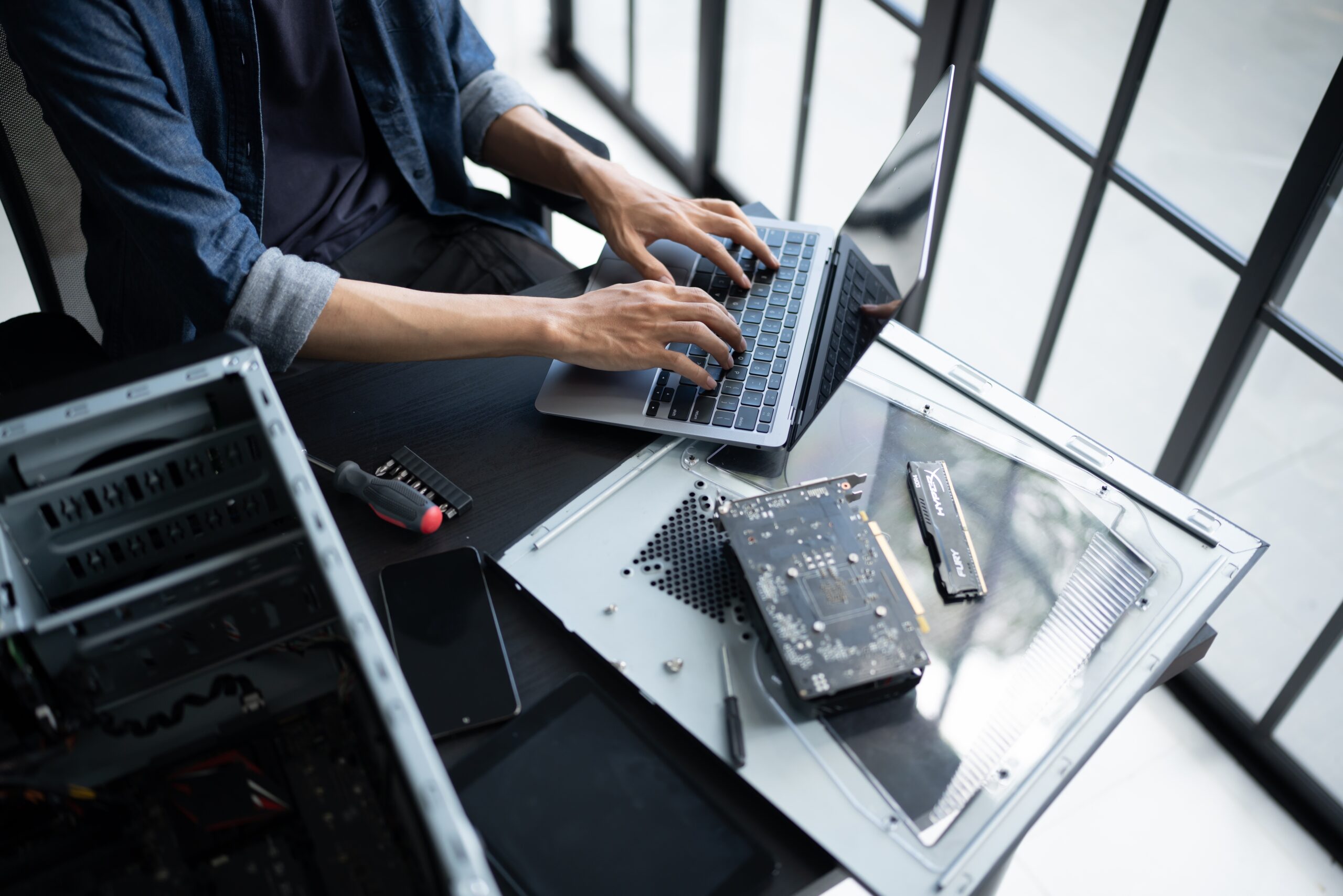 Photo of an engineer working on a laptop whilst carrying out physical repairs to a computer server 